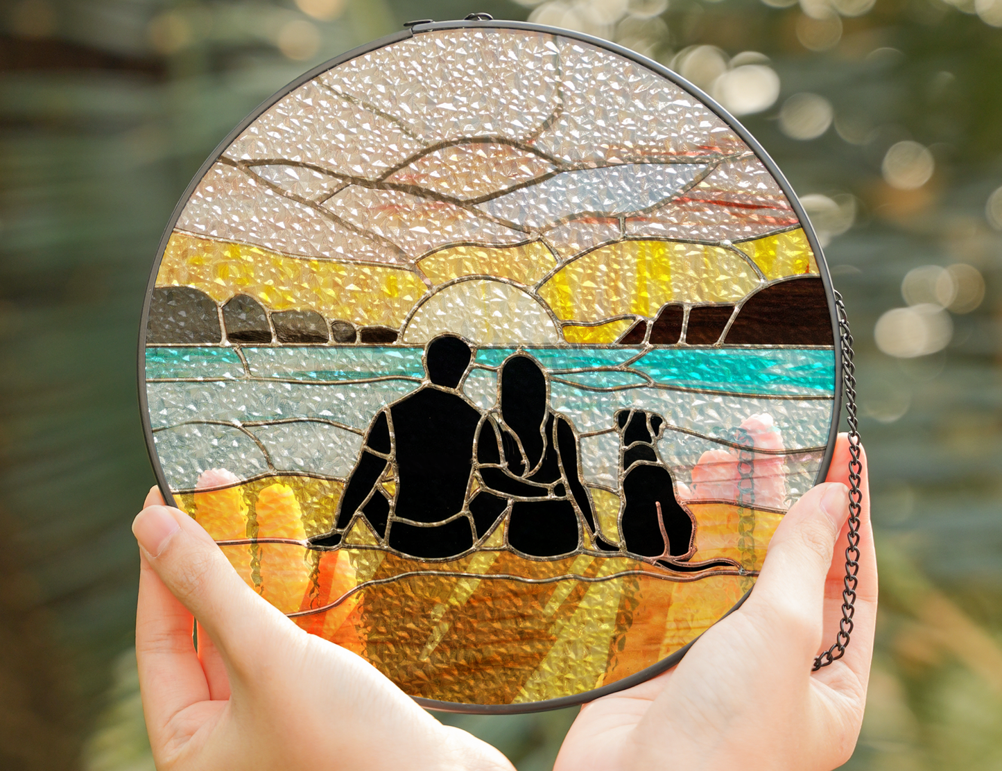 couple and dog at beach sunrise suncatcher held in hands above water