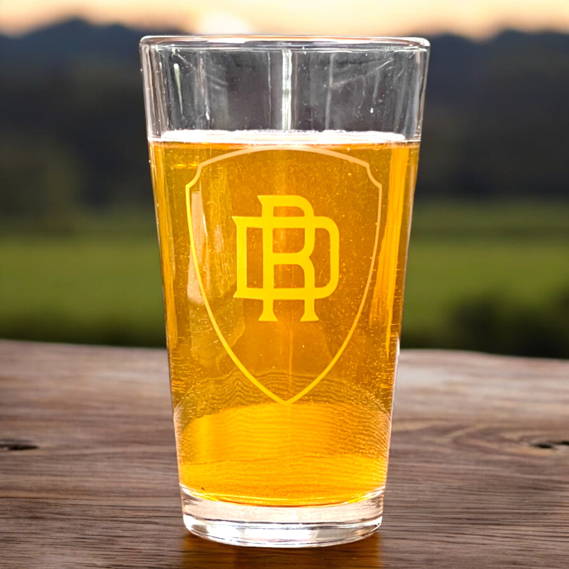 personalized pint glass with shield and monogram on a wood table